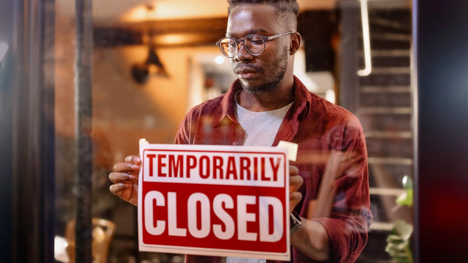 Business owner putting up sign on store that says temporarily closed